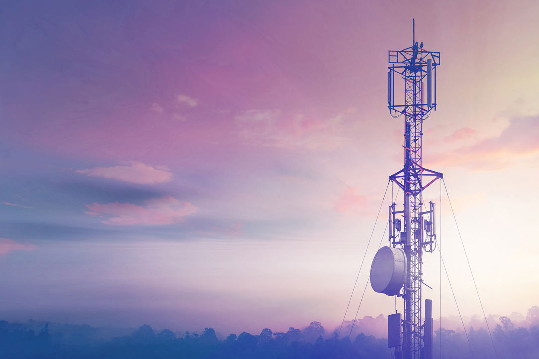 A large telecoms tower looms above a forested horizon at sunset